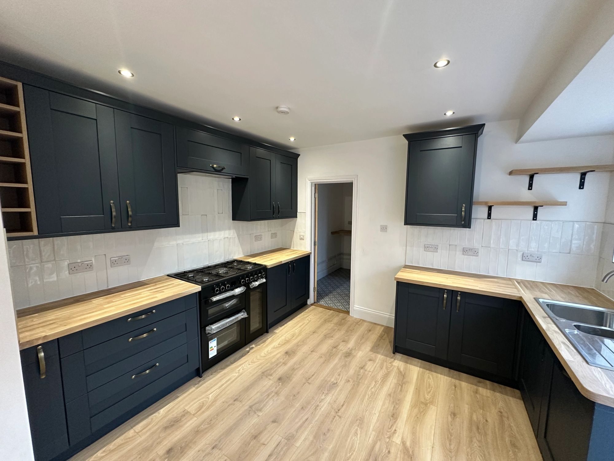 A finished kitchen with navy shaker units, solid oak worktops, white metro tiles and a range cooker.