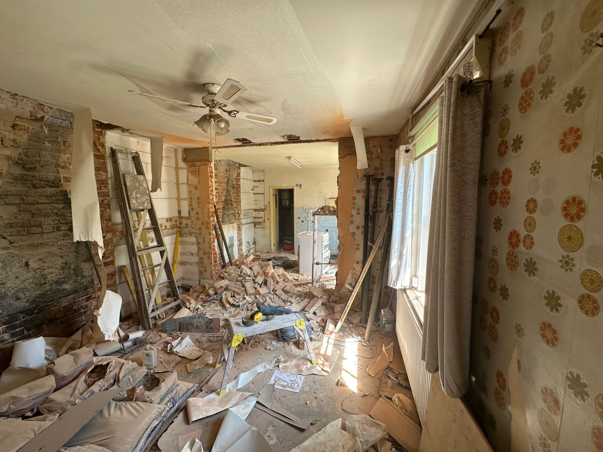 A room stripped back to brick with acrow props supporting the ceiling while a wall is taken out.